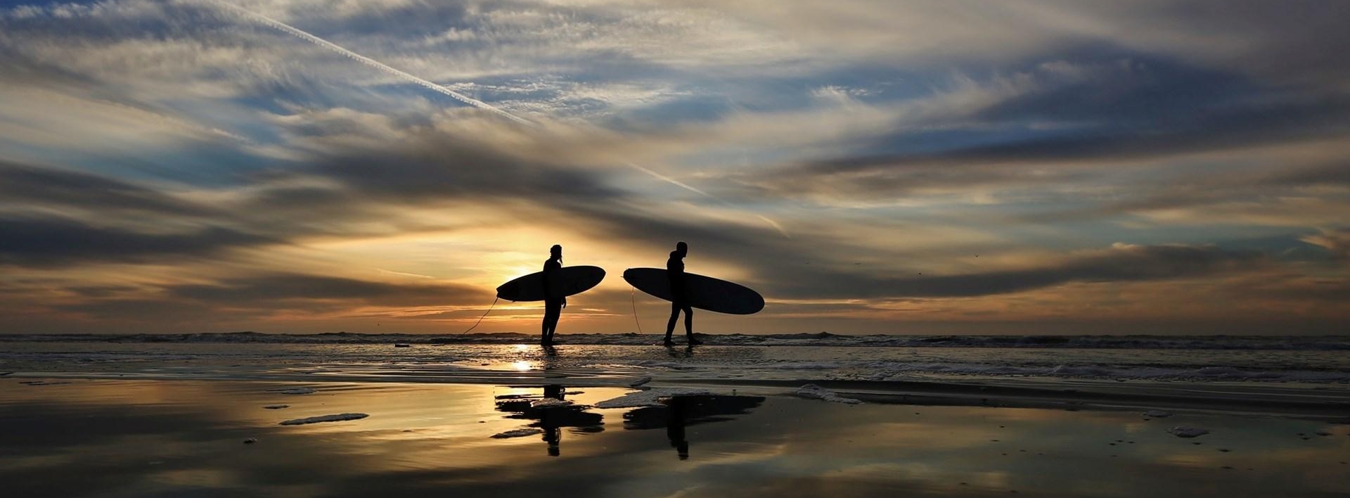 Surfers bij zonsondergang op het strand bij Egmond aan Zee